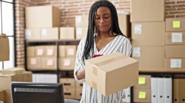 Afrika kökenli Amerikalı kadın ecommerce işçisi ofisinde akıllı telefon ile bilgisayar tarama paketi kullanıyor.