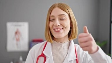 Genç sarışın kadın doktor klinikte başparmağını kaldırıyor.