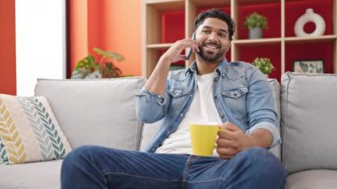 Afro-Amerikalı adam akıllı telefondan konuşuyor evde kahve içiyor.
