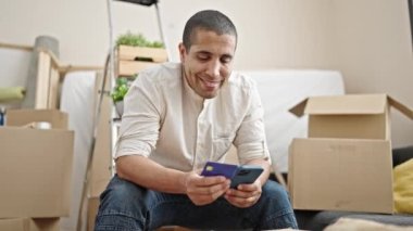 Genç İspanyol adam yeni evinde akıllı telefon ve kredi kartıyla alışveriş yapıyor.