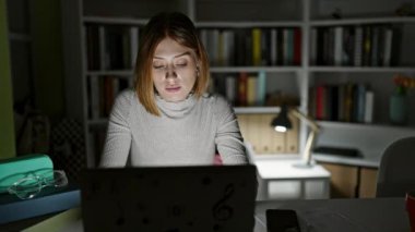 Kütüphanede dizüstü bilgisayar ve akıllı telefon kullanan genç sarışın kız öğrenci.