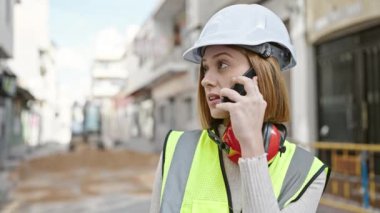 Sarışın genç bir mimar sokakta akıllı telefondan konuşuyor.