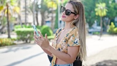 Genç sarışın kadın parkta akıllı telefondan müzik dinliyor.