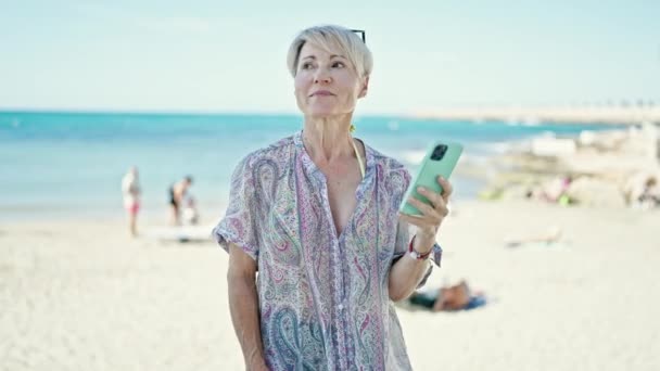 中年金发女性游客使用智能手机环视海滩 — 图库视频影像