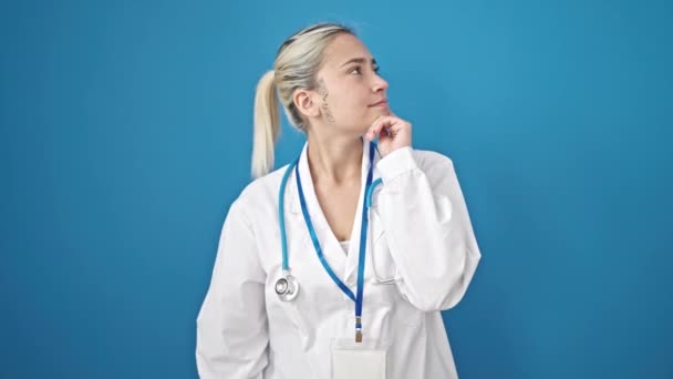 年轻美丽的惊慌失措的女医生站在那里 满腹狐疑地思量着孤立的蓝色背景 — 图库视频影像