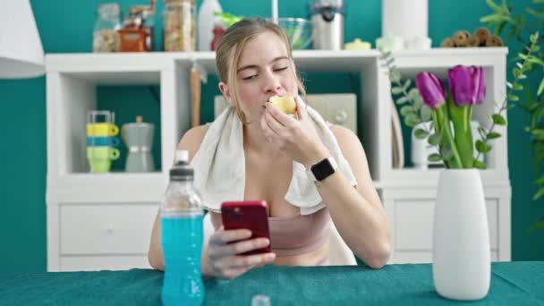 Ung Blond Kvinna Bär Sportkläder Äta Äpple Med Hjälp Smartphone — Stockvideo