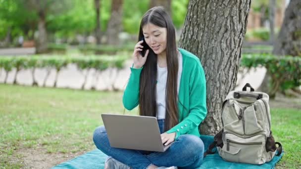 公園でラップトップを使用してスマートフォンで話している若い中国人女性 — ストック動画