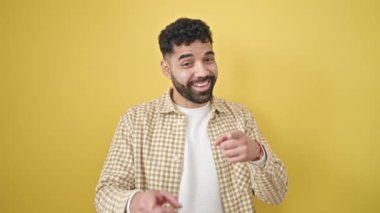 Genç İspanyol adam gülümsüyor. Kendine güveni tam. İzole edilmiş sarı arka planda kamerayı işaret ediyor.