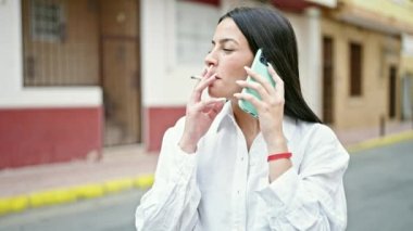 Genç, güzel İspanyol kadın akıllı telefonda konuşuyor sokakta sigara içiyor.