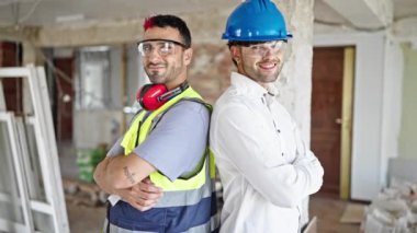 İki adam mimar ve mimar gülümsüyor. İnşaat alanında kollarını kavuşturmuş duruyor.