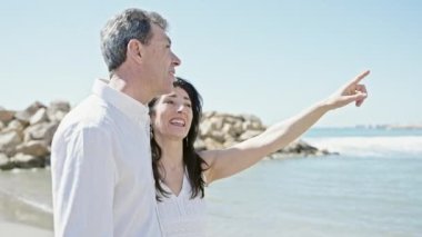 Kıdemli erkek ve kadın çift gülümsüyor deniz kenarında parmaklarıyla işaret ederek kendine güveniyorlar