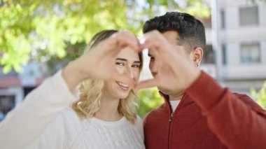 Kadın ve erkek, parktaki elleriyle kalp hareketi yaparak gülümsüyor.