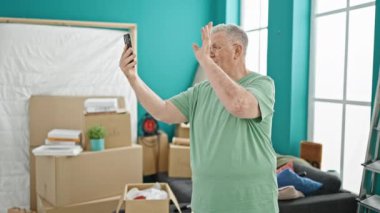 Orta yaşlı, kır saçlı bir adam yeni evinde video görüşmesi yapıyor.