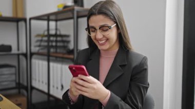 Ofiste çalışan genç ve güzel İspanyol iş kadını akıllı telefon kullanıyor.