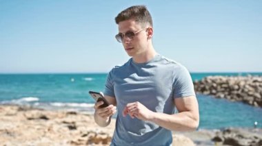 Genç İspanyol turist deniz kenarında akıllı telefonuyla selfie çekiyor.