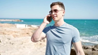 Genç İspanyol turist gülümseyerek deniz kenarında akıllı telefondan konuşuyor.