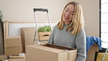 Genç sarışın kadın yeni evinde kendine güvenen bir paket tutuyor.