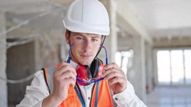 Kafkasyalı genç bir mimar gülümsüyor inşaat alanında bardakları çıkarıyor.