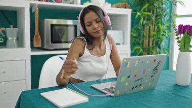 Afro-Amerikalı kadın yemek odasında defterde müzik dinliyor.