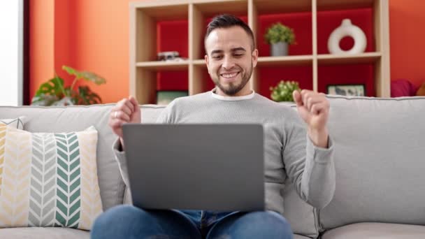 Латиноамериканець Використовує Ноутбук Святкуючи Сидіння Дивані Вдома — стокове відео