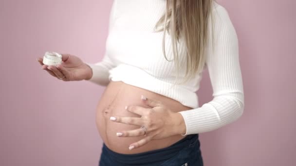 Jonge Zwangere Vrouw Aanbrengen Huidverzorging Crème Buik Geïsoleerde Roze Achtergrond — Stockvideo