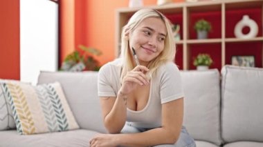 Young beautiful hispanic woman sitting on sofa with doubt expression at home