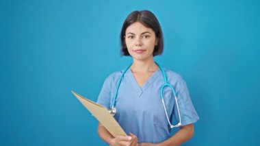 Genç, güzel, İspanyol bir doktor elinde mavi arka planda gülümseyen bir belge tutuyor.