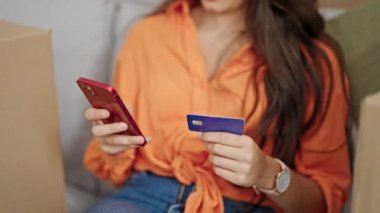 Genç, İspanyol bir kadın akıllı telefon ve kredi kartıyla alışveriş yapıyor. Yeni evindeki kanepede oturuyor.