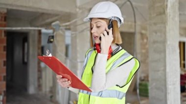 Genç sarışın mimar inşaat alanında akıllı telefon okuyarak konuşuyor.