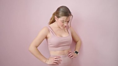 Spor kıyafetleri giyen genç sarışın kadın pembe arka plana bakıyor.