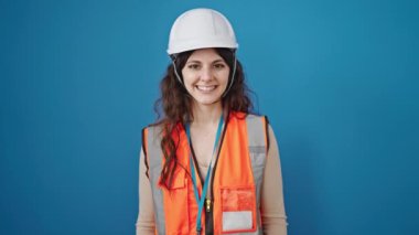 Genç, güzel İspanyol kadın inşaatçı gülümseyen, kendine güvenen, izole edilmiş mavi arka planda el hareketi yapan.