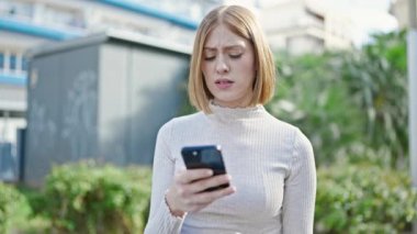 Parkta akıllı telefon kullanan genç sarışın kadın.