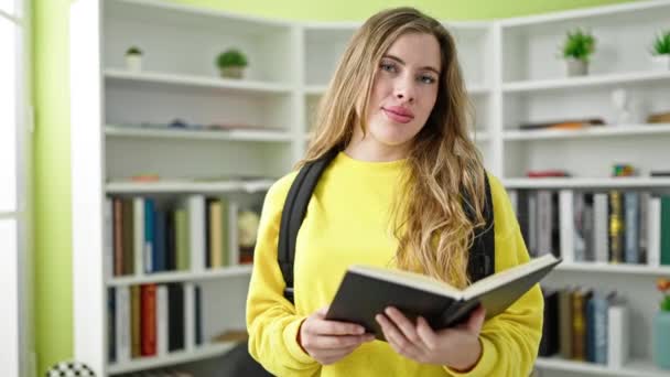 Young Blonde Woman Student Wearing Backpack Reading Notebook Library University — Stock Video