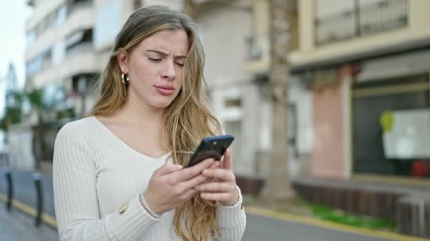 年轻的金发女人在街上用带有严肃表情的智能手机 — 图库视频影像