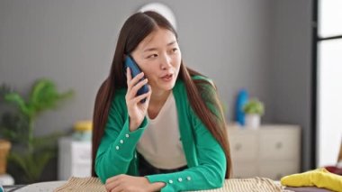 Genç Çinli kadın akıllı telefondan konuşuyor çamaşır odasında ütü masasına yaslanıyor.