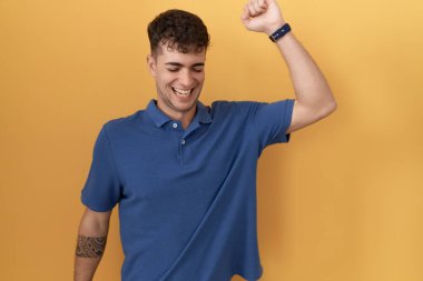 Young hispanic man standing over yellow background dancing happy and cheerful, smiling moving casual and confident listening to music 