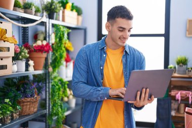 Çiçekçide dizüstü bilgisayar kullanarak gülümseyen İspanyol bir çiçekçi.