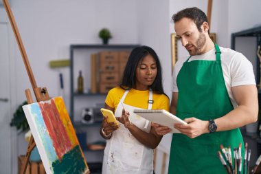 Man and woman artists using smartphone holding notebook at art studio
