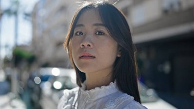 Young chinese woman standing with serious expression at street