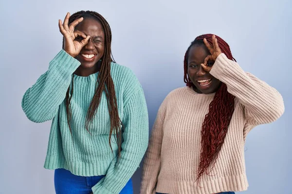 Dwie Afrykańskie Kobiety Stojące Nad Niebieskim Tłem Robiące Gest Uśmiechem — Zdjęcie stockowe