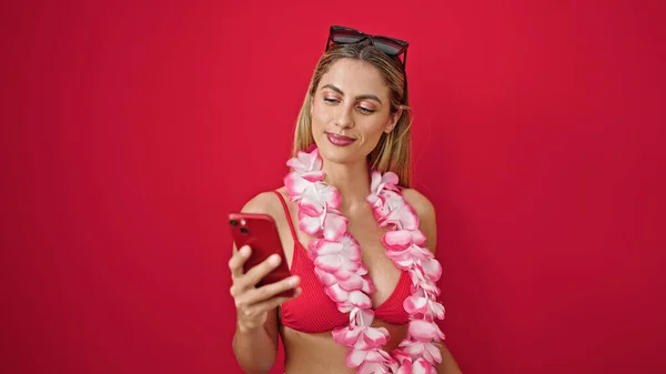 若いですブロンド女性観光客を使用してスマートフォン笑顔上の隔離された赤の背景 — ストック写真
