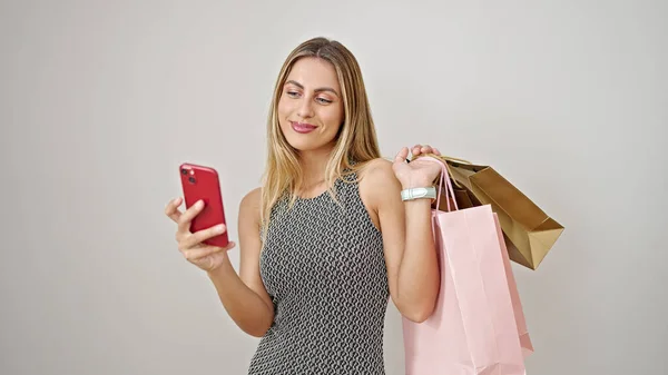 Młoda Blondynka Trzyma Torby Zakupy Pomocą Smartfona Białym Tle — Zdjęcie stockowe