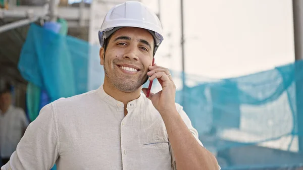 若いヒスパニック系の男建築家が路上で笑顔でスマートフォンについて話す — ストック写真