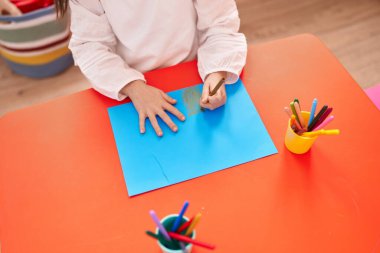 Anaokulunda masada oturan sevimli İspanyol kız öğrenci defterine çizim yapıyor.