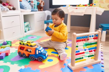 Anaokulunda yerde oturan sevimli İspanyol çocuk araba oyuncağıyla oynuyor.