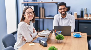 Man and woman business workers using laptop sitting with arms crossed gesture at office