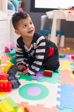 Anaokulunda yerde oturan sevimli İspanyol çocuk araba oyuncağıyla oynuyor.