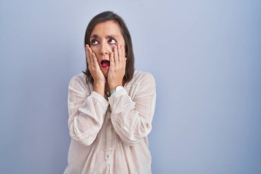 Orta yaşlı İspanyol kadın mavi arka planda duruyor. Yorgun eller yüzünü, depresyonunu ve üzüntüsünü örtüyor. Sorunları yüzünden üzgün ve sinirli. 