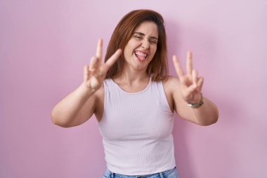 Pembe arka planda dikilen esmer kadın her iki elinde parmaklarını göstererek gülümseyerek zafer işareti yapıyor. İki numara.. 