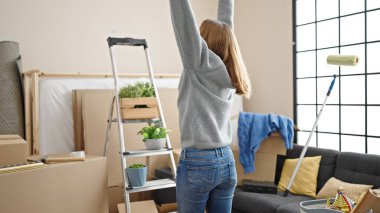 Yeni evinde kolları açık genç sarışın bir kadın.